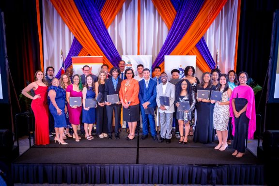 Group photo of Proud of Them Youth Awards 2025 honourees and organisers standing on stage holding certificates at the gala ceremony in the Kimpton Seafire ballroom, Cayman Islands.